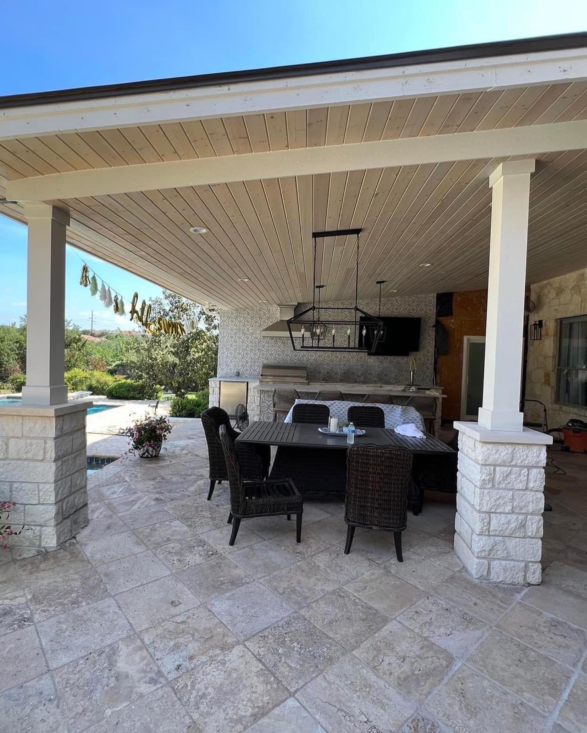 Finished covered patio with stone columns, dining table and outdoor kitchen beside a pool