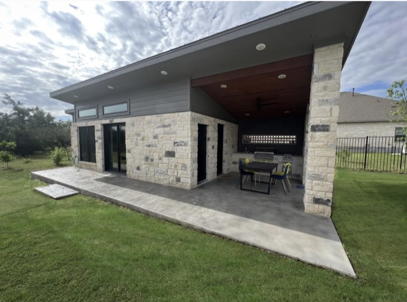 Stone pool house with covered dining patio, wood ceiling and sliding glass doors connecting indoor and outdoor space