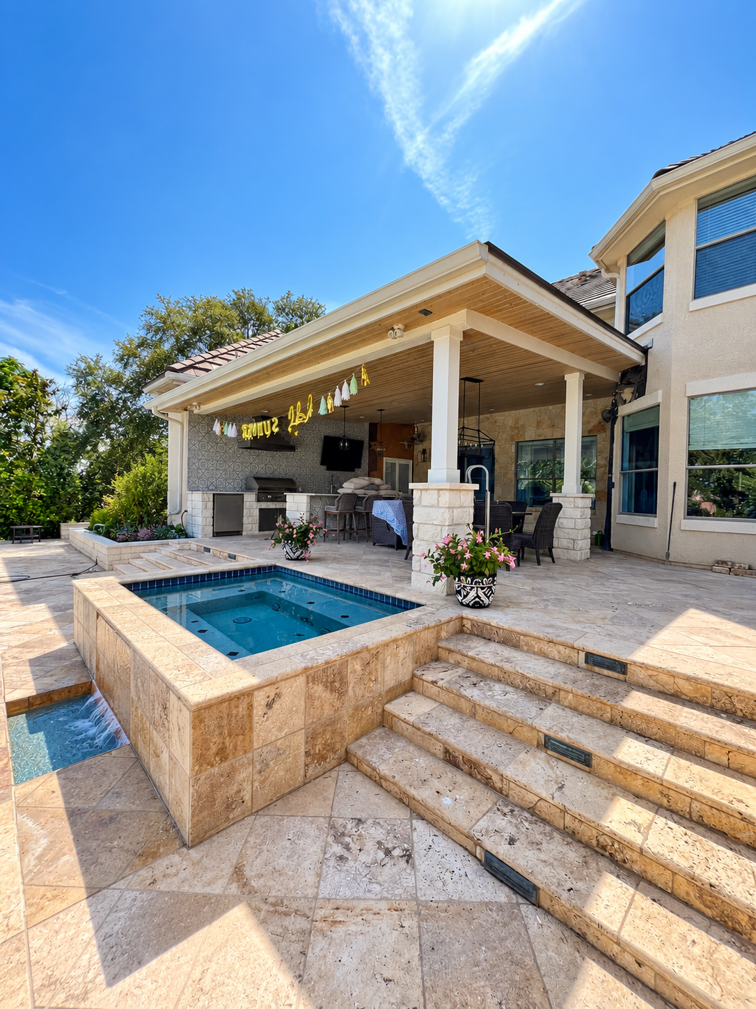 Poolside covered patio with an outdoor kitchen, integrated hot tub, travertine decking and steps leading into a swimming pool