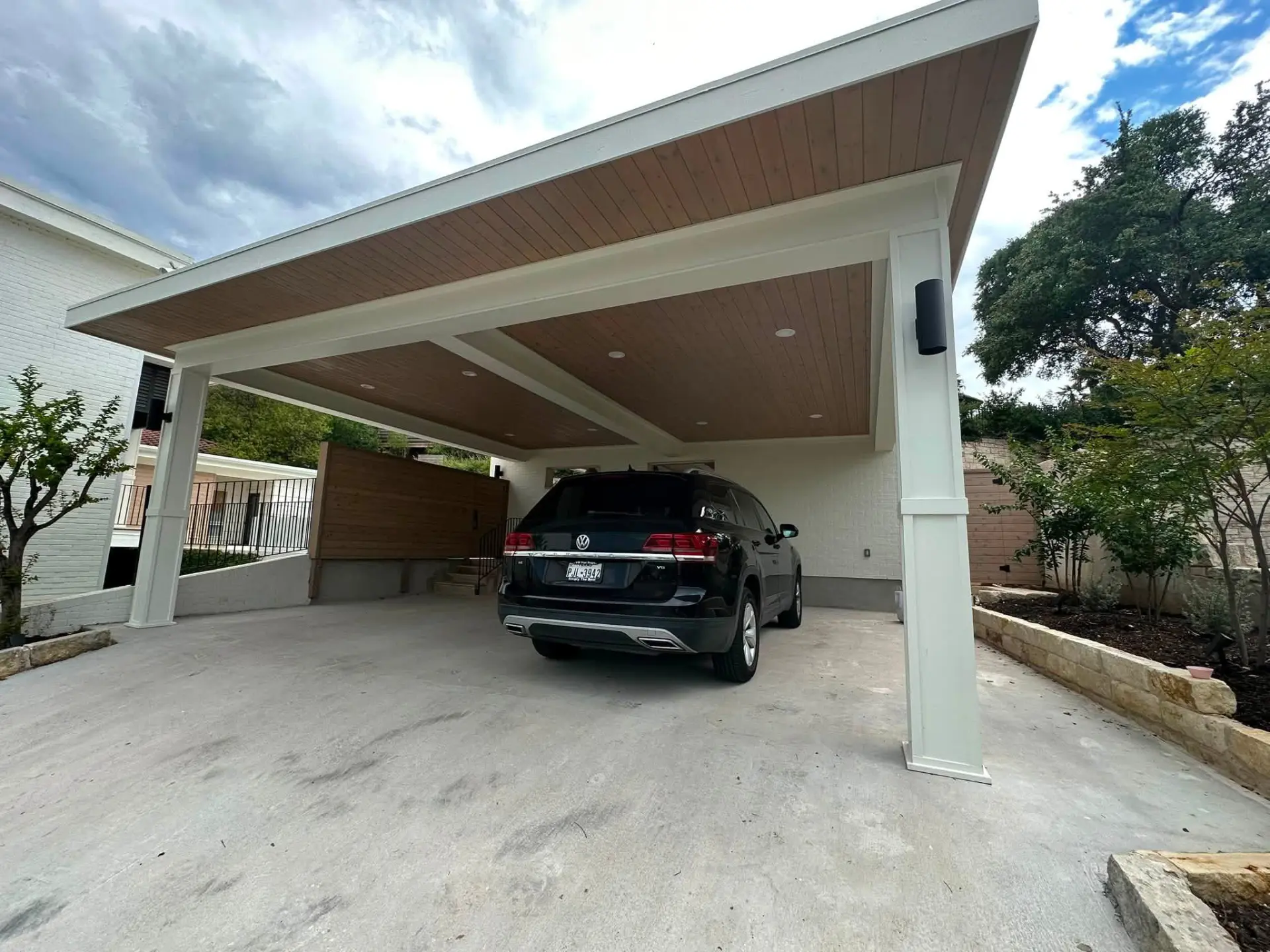 Custom carport with a finished wood ceiling and white supports, covering a parked SUV