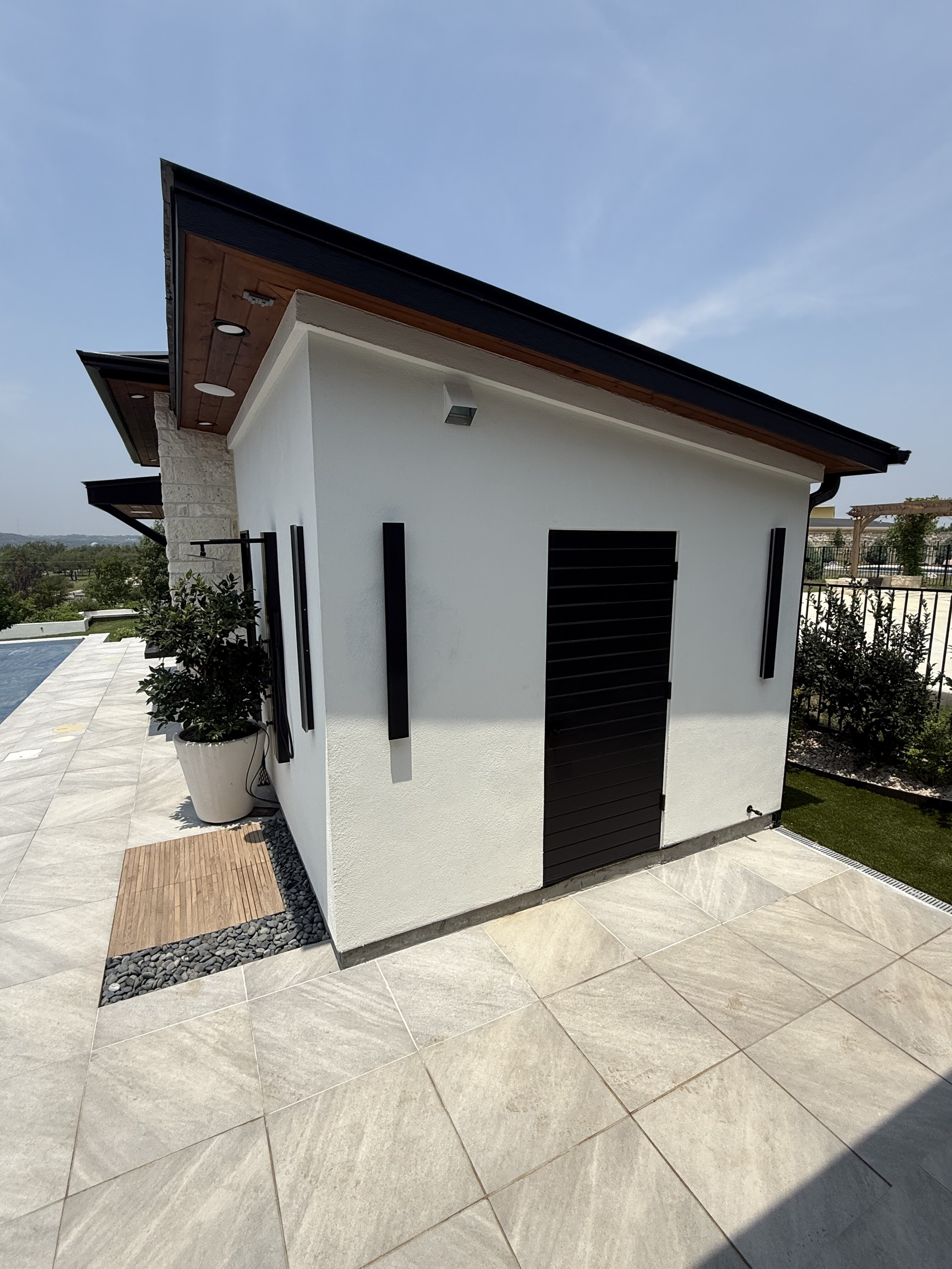Exterior of a finished pool-house restroom with dark shutters, stucco walls and poolside decking