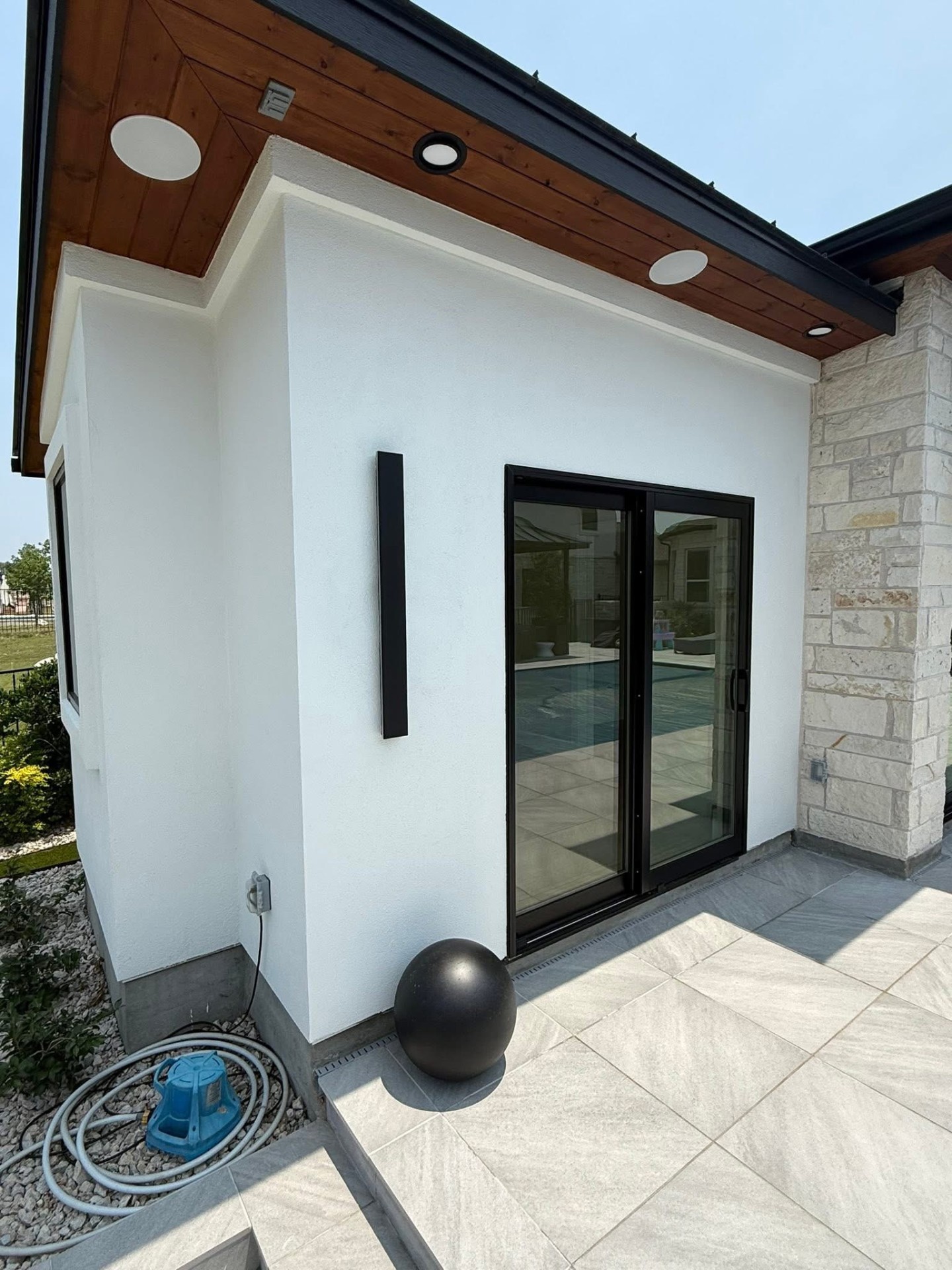 White stucco casita exterior with black-framed sliding doors, wood soffit, and a stone column
