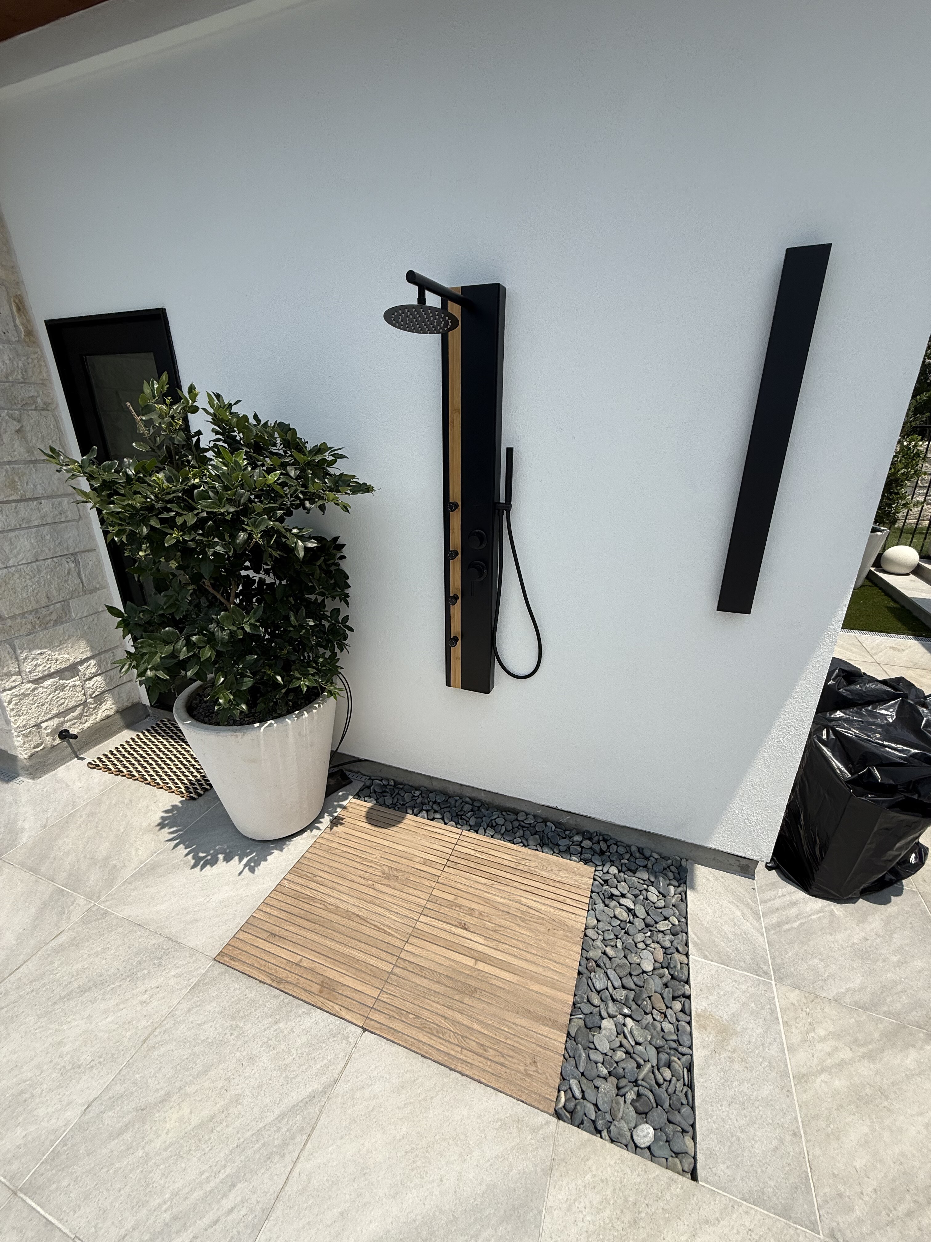 Modern outdoor shower panel mounted on a pool-house wall with stone accent and tiled deck
