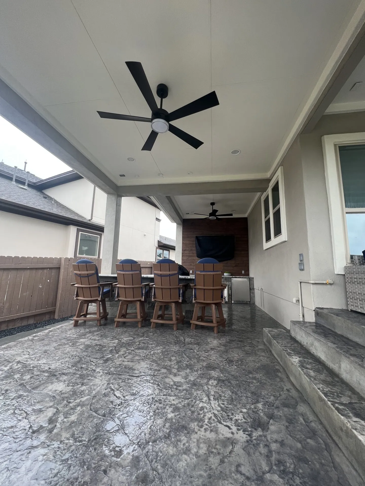 Furnished open covered terrace with seating, ceiling fans and an entertainment wall