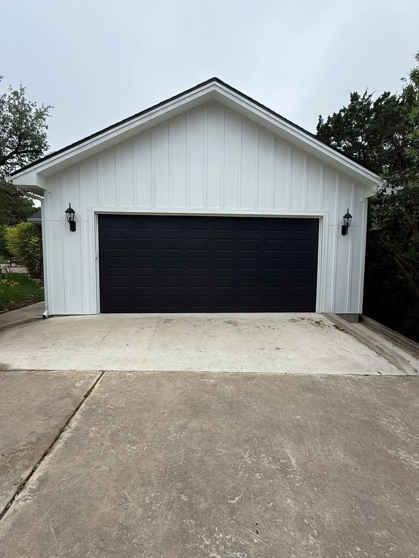 Custom detached garage with white board-and-batten siding and a black garage door
