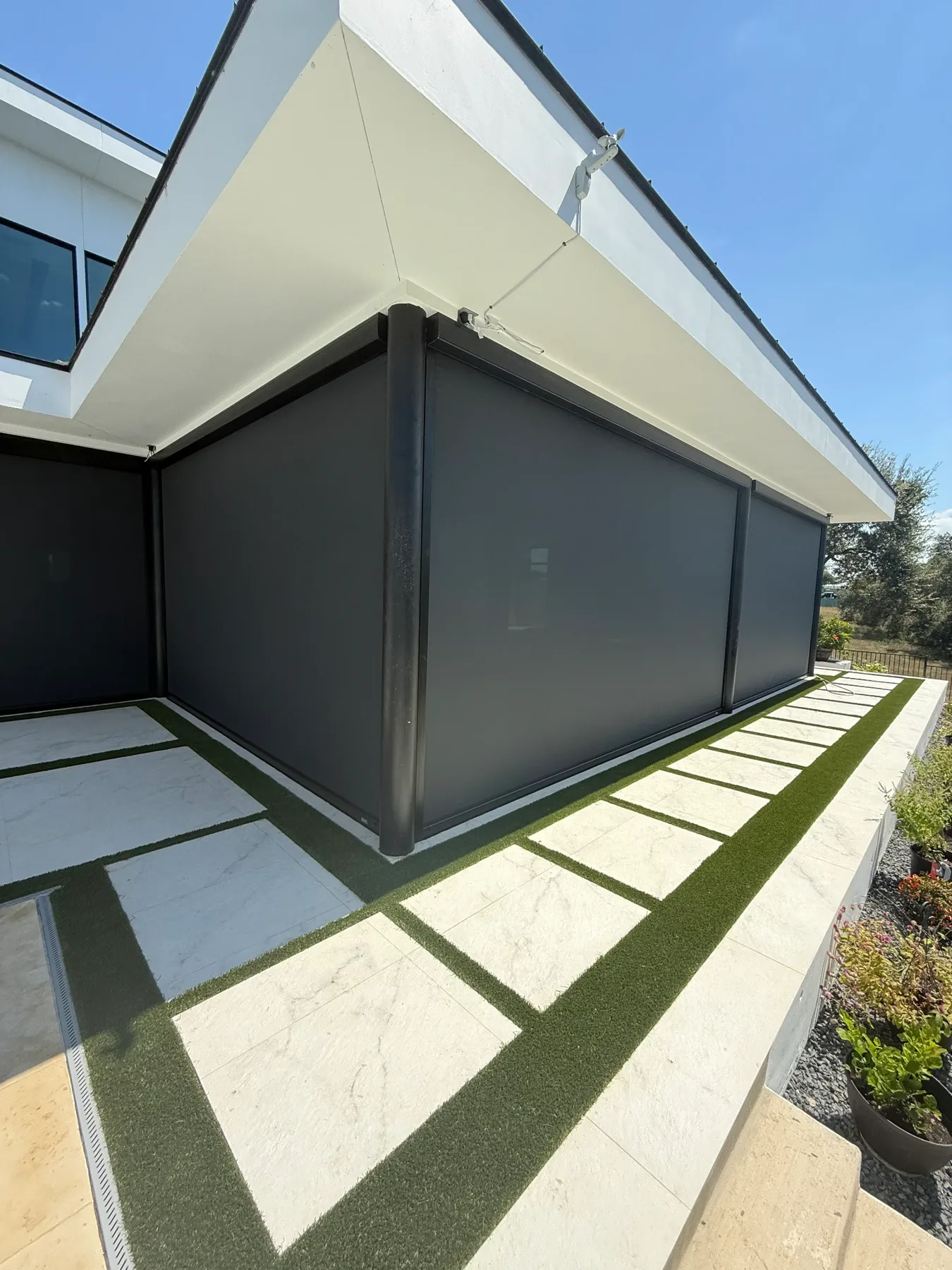 Motorized screens wrapping a corner patio above large square stone pavers set in turf