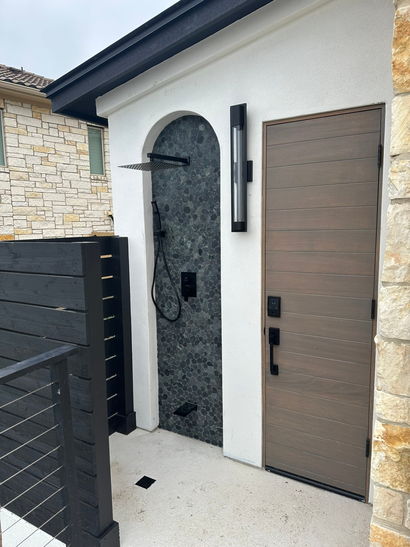 Outdoor pool-house shower and changing area with stone tile accent wall, rainfall shower and modern fixtures