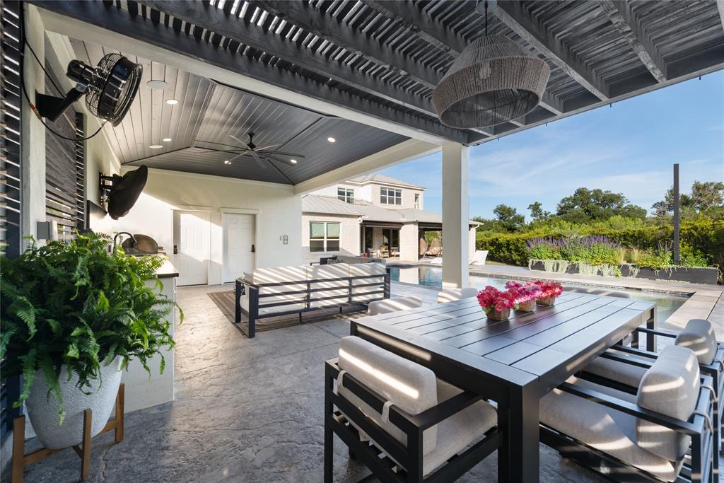Covered poolside dining and lounge area with vaulted ceiling, modern fixtures and sightlines to the home and pool