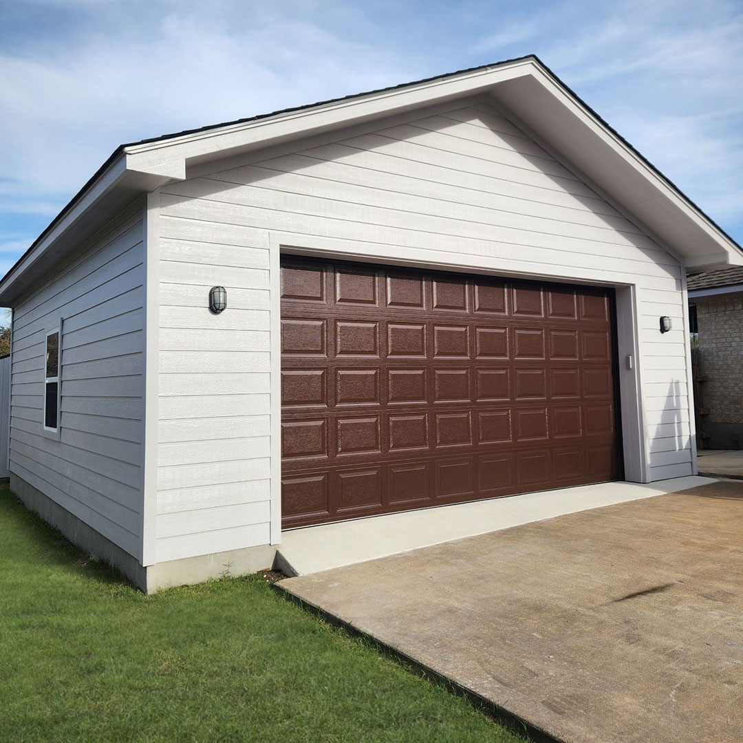 Custom detached garage with white board-and-batten siding and a brown overhead door