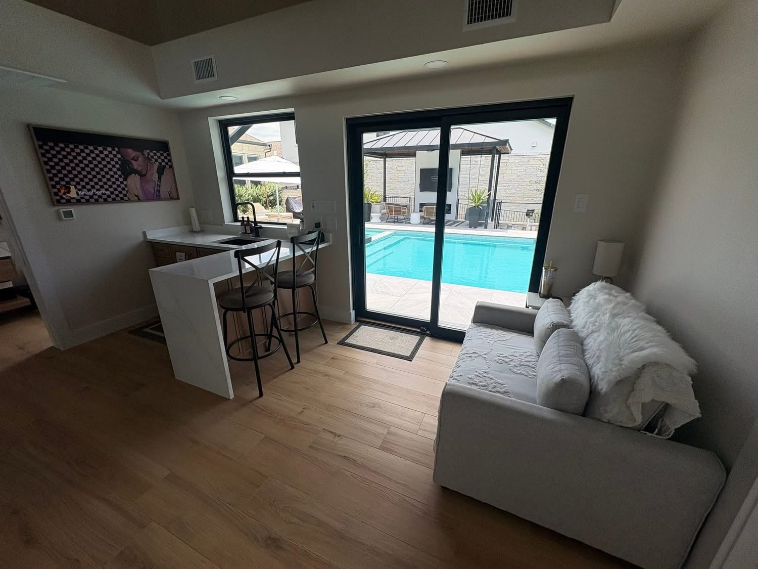Interior of a finished pool house with bar seating, sofa and sliding glass doors opening to a turquoise swimming pool