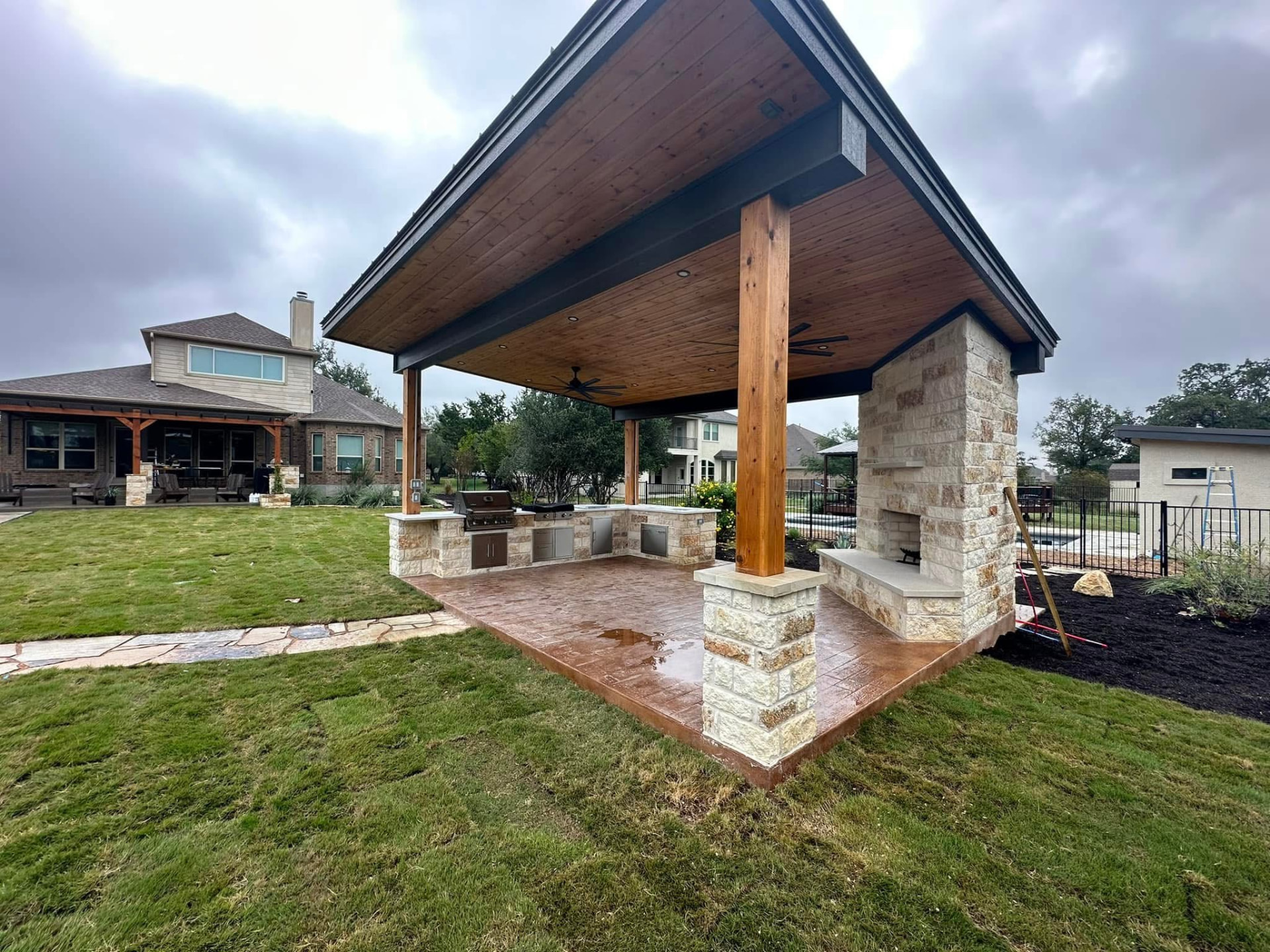 Freestanding pavilion with stone fireplace, wood ceiling, outdoor kitchen and stamped concrete patio