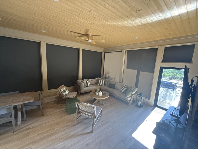 Interior of a finished pool house with a wood ceiling, comfortable seating, dining area and retractable screen panels opening to the pool