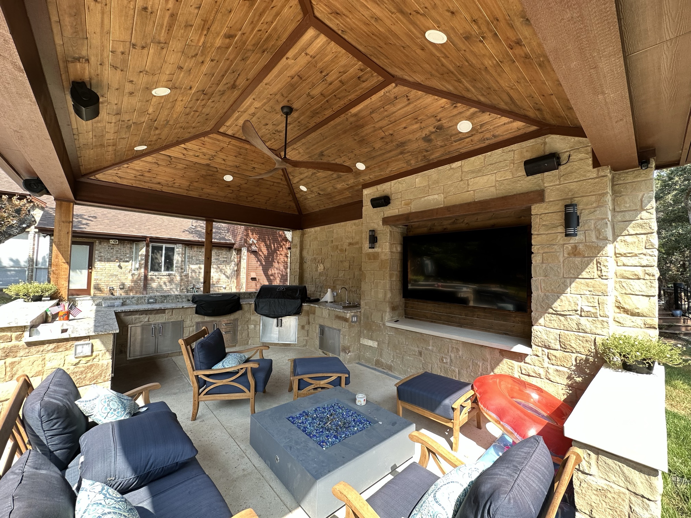 Covered hexagonal patio with an outdoor kitchen, television and fire table