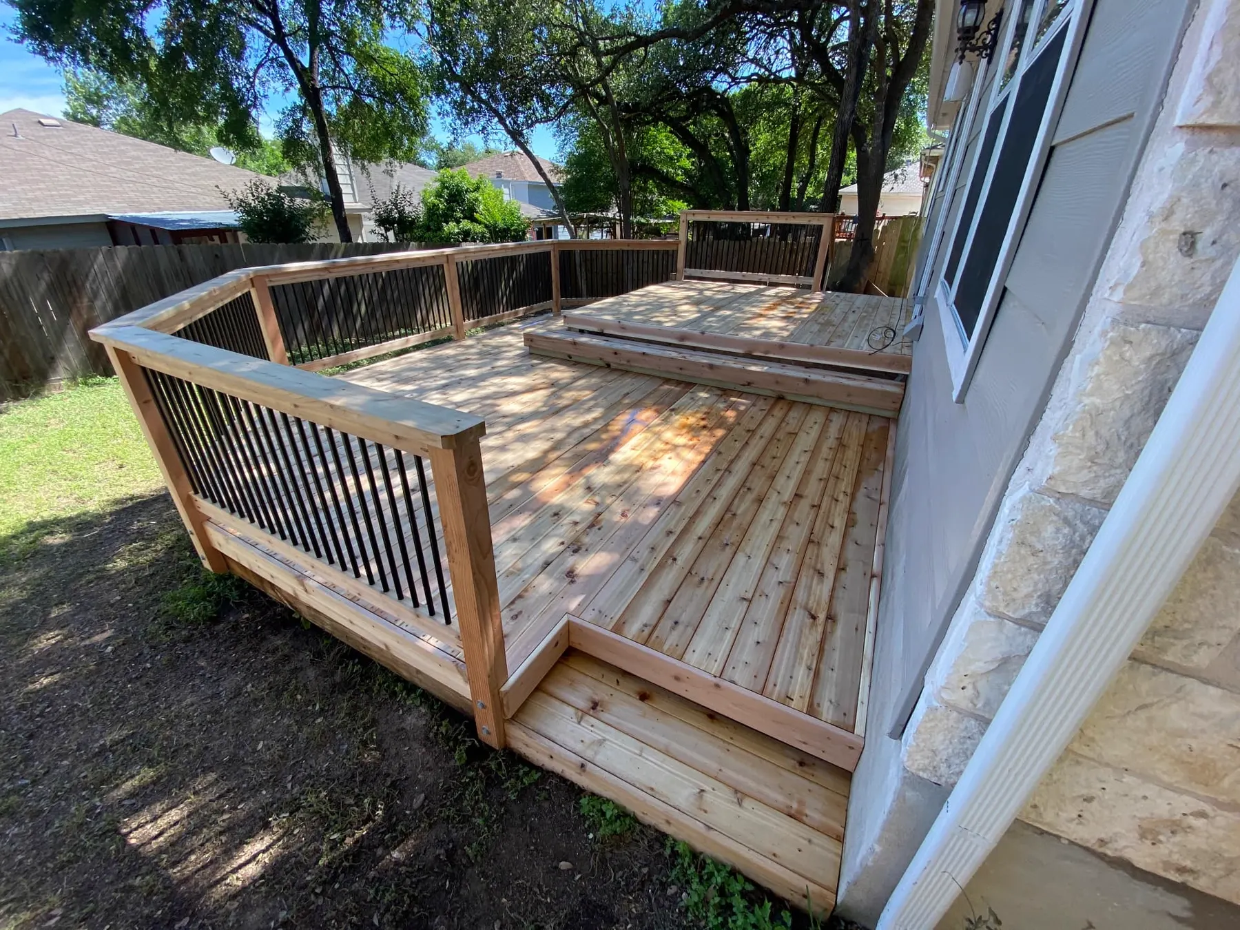 Custom cedar deck and railing structure built into a shaded backyard