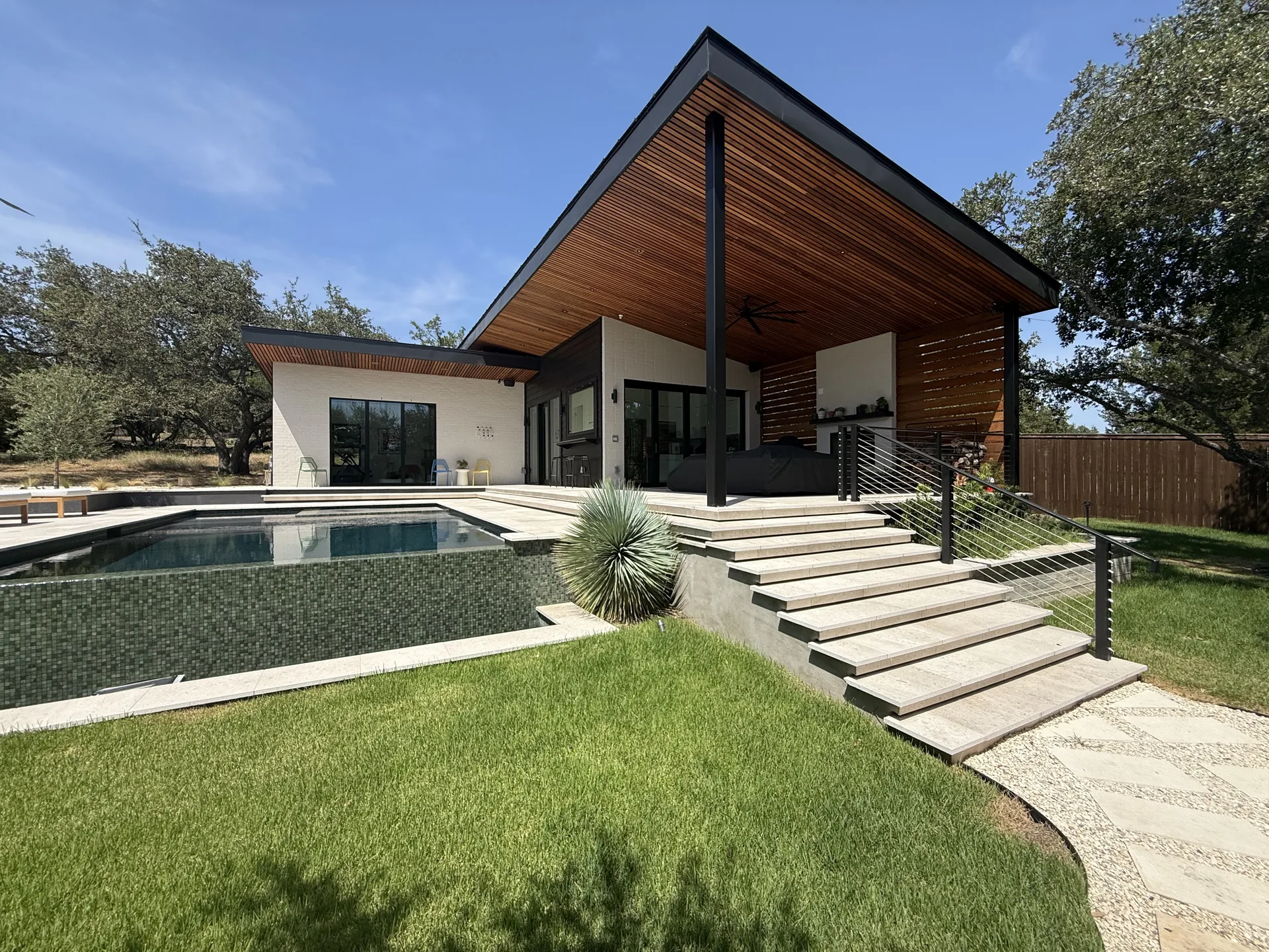 Finished TWT outdoor living structure with a wood soffit, broad gabled roof, pool and stepped terrace