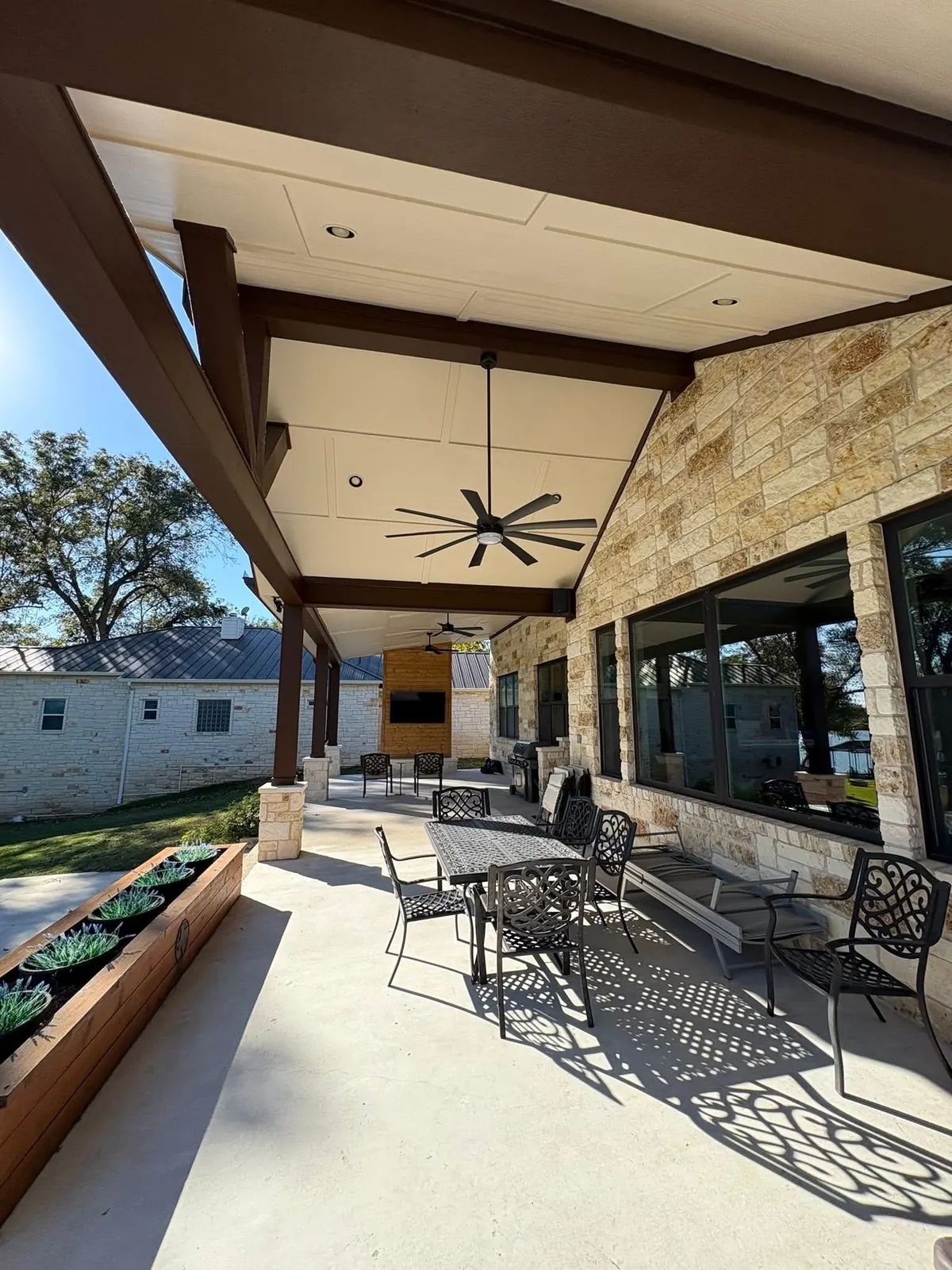 Covered patio with dark stained beams over a stone dining terrace and planters