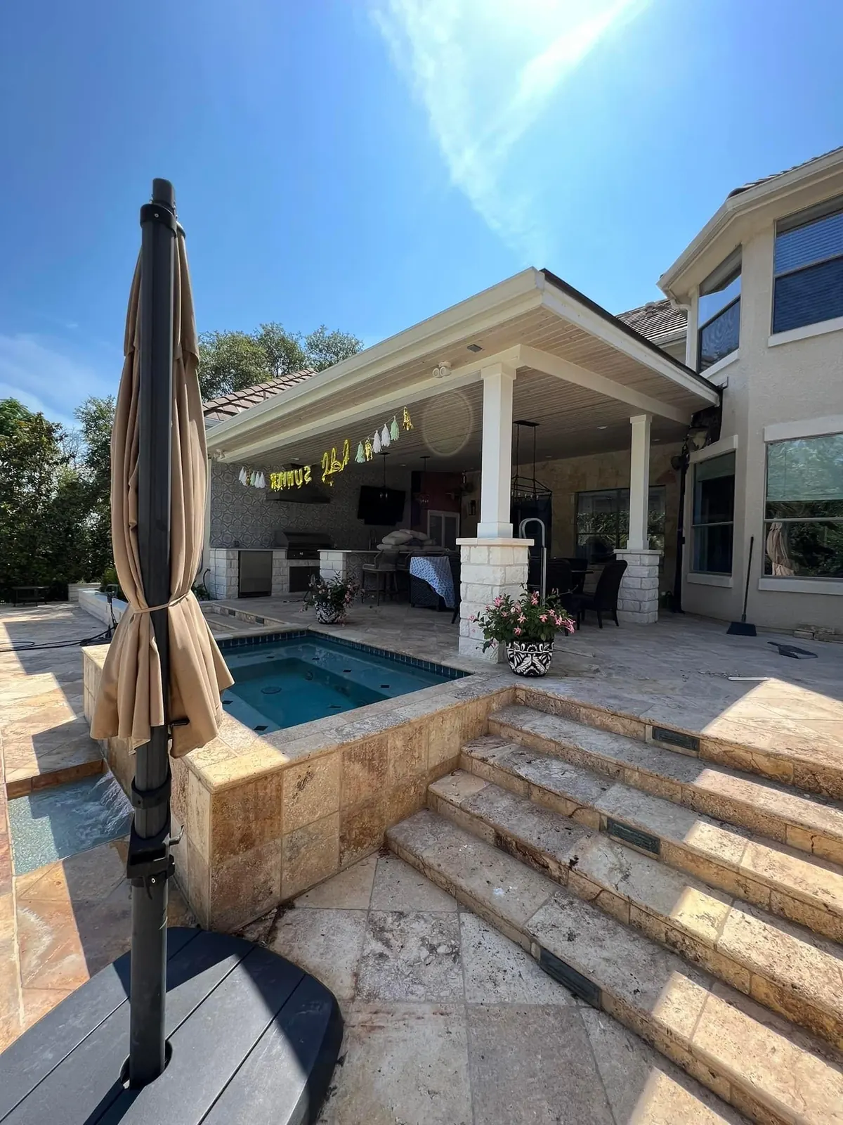 Covered patio and outdoor kitchen beside a pool with travertine steps