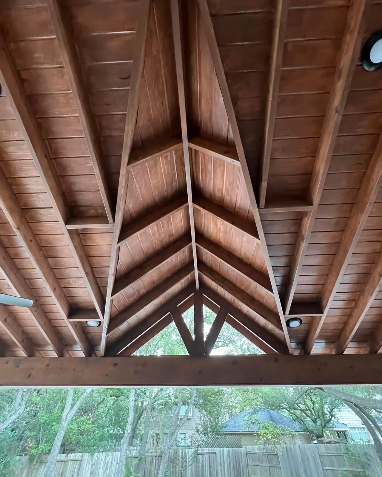 Detail of an exposed stained timber truss and decking ceiling on a covered patio