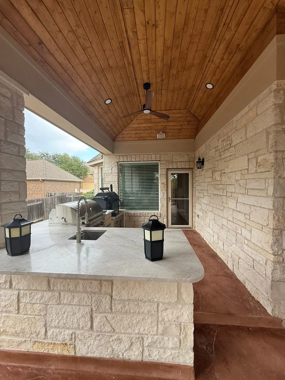 Vaulted wood ceiling above a stone outdoor kitchen counter with lanterns