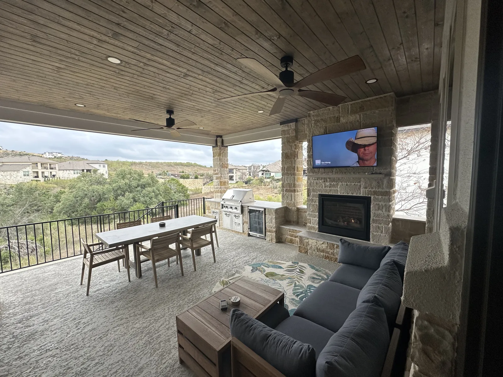 Covered outdoor living space with a stone fireplace, dining table, built-in grill and a hill country view