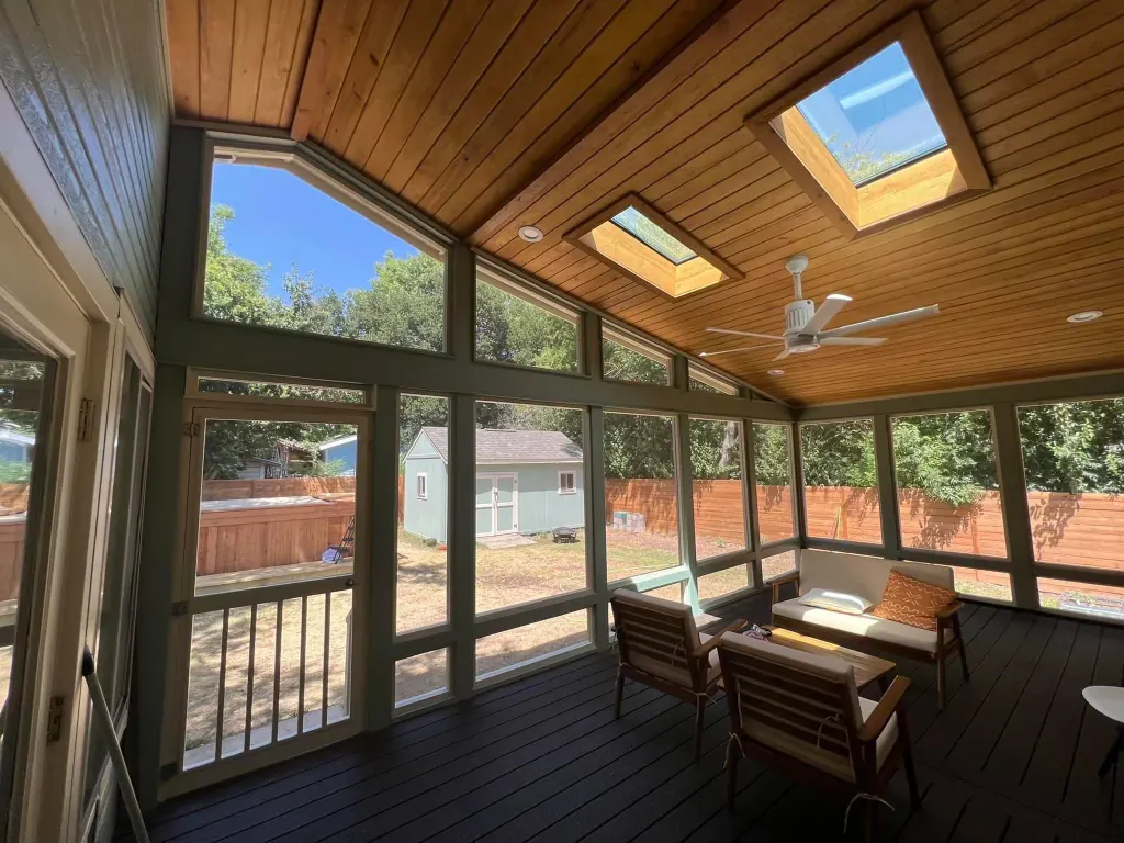 Interior of a fixed screen enclosure with a stained wood ceiling, skylights and a dark deck floor