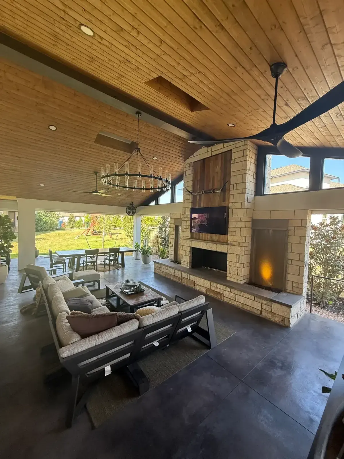 Covered outdoor living room with stone fireplace, vaulted wood ceiling and adjacent dining area at a Rough Hollow project