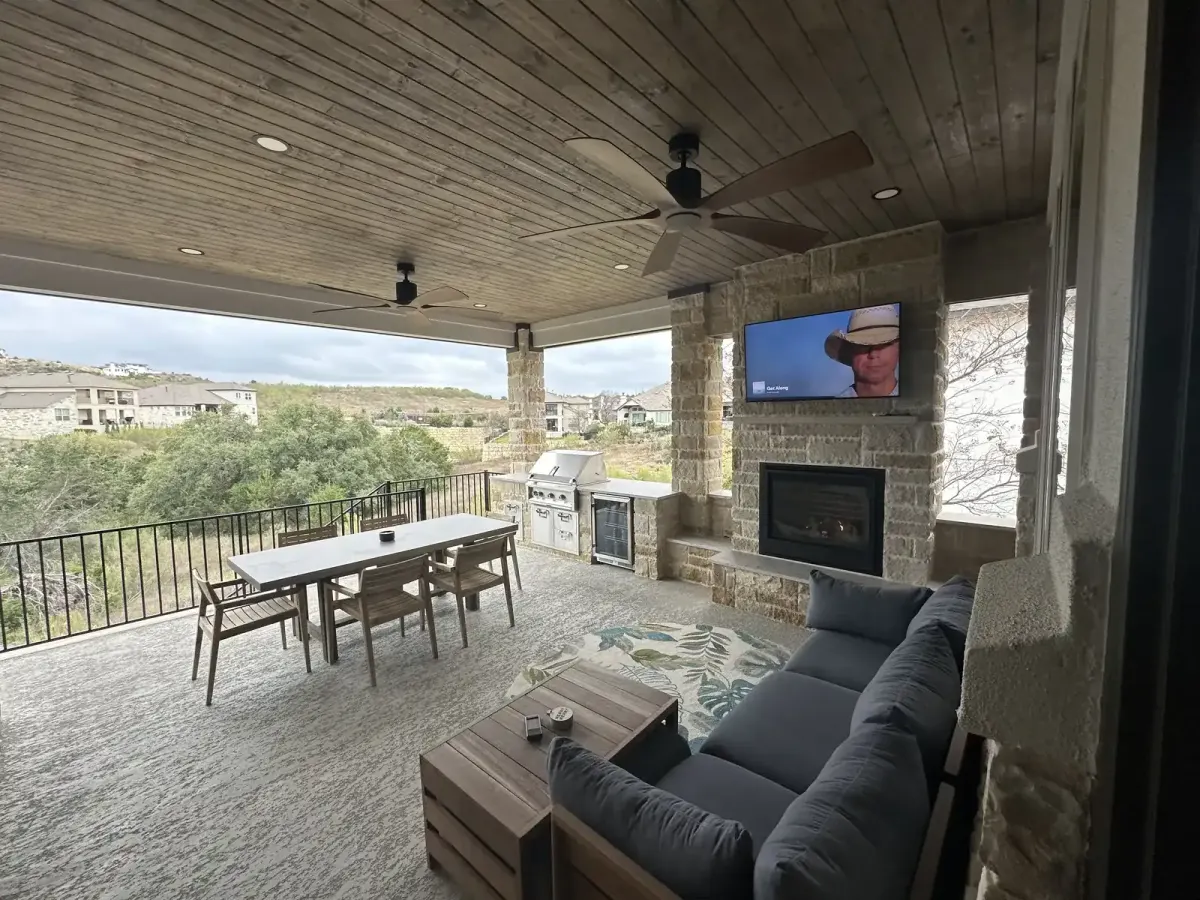 Covered outdoor living space with a stone fireplace, dining table, built-in grill and a hill country view